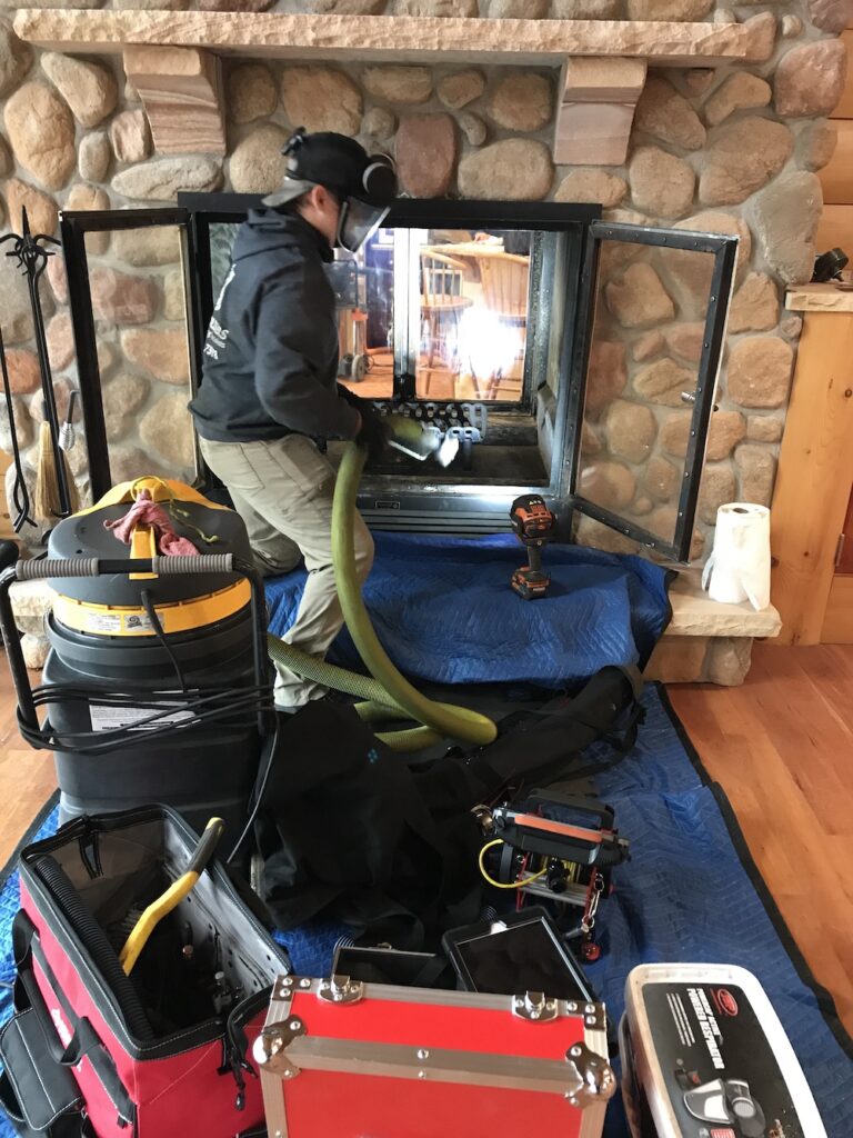 Technician vacuuming and cleaning a fireplace with protective coverings.
